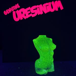 Könnte beinhalten: Eine fluoreszierende, limettengrüne Torso-Skulptur, die unter ultraviolettem Licht leuchtet. Über der Skulptur ist der Text GENUINE URESINIUM in leuchtend rosa Buchstaben vor einem dunklen Hintergrund zu sehen, was die reaktiven Eigenschaften betont.