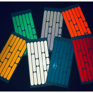 May include: Assortment of reflective bike spoke stickers in various colours, including orange, green, white, grey, blue, and red. Each sticker sheet features a repeating pattern of oval shapes.