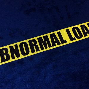 Puede incluir: Una señal de advertencia amarilla y negra con el texto "ABNORMAL LOAD" sobre un fondo azul.