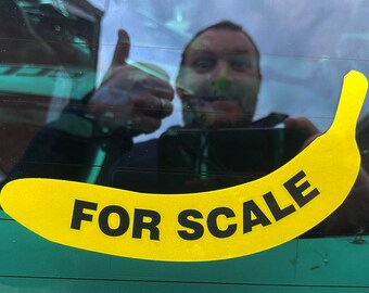 May include: A yellow banana sticker with the text "FOR SCALE" on a car window.