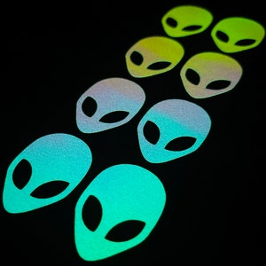 Puede incluir: Un conjunto de ocho pegatinas de cabeza de extraterrestre iridiscentes en un degradado de verde, amarillo y azul. Las pegatinas están dispuestas en una línea vertical, con la más verde en la parte superior y la más azul en la parte inferior.