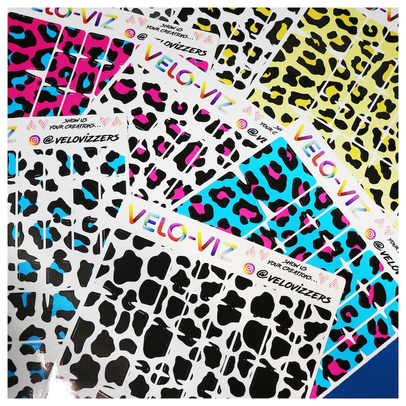 May include: Assortment of colorful leopard print vinyl stickers with the text "Show us your creations... @VeloVizzers" on several of the stickers. The stickers are arranged in a random pattern.