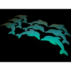 以下が含まれることがあります： 黒い背景に、ティール色のイルカの切り抜きが並んでいます。イルカは、さまざまなサイズと向きで、流れるようなパターンに配置されています。ティール色はグラデーション効果があり、明るい色合いから暗い色合いに変化しています。