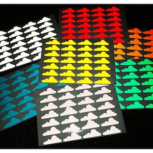 Op de afbeelding: Zes vellen met glow-in-the-dark wolkenstickers in verschillende kleuren, waaronder wit, geel, oranje, rood, blauw en groen.