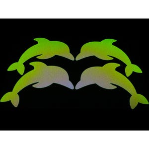 以下が含まれることがあります： 黒い背景に、緑と黄色のイルカのシルエットが4つ。イルカは対になっており、互いに向き合っています。色のグラデーションが奥行きを表現。対称的で目を引くデザインです。