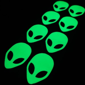 May include: Eight glow-in-the-dark green alien head stickers. The stickers are arranged in a vertical line, with the top sticker at the top of the image and the bottom sticker at the bottom of the image.