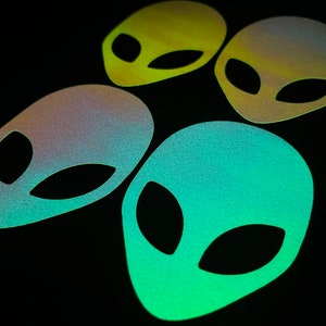 May include: Four iridescent alien head stickers in green, blue, and yellow. The stickers are shaped like alien heads with large black eyes.