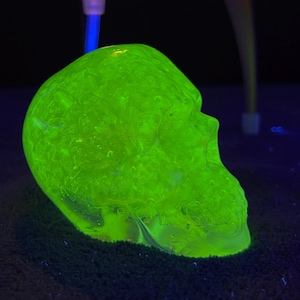 Peut inclure: Une figurine de crâne vert fluorescent. Le crâne est éclairé par une lumière vert néon vive, créant un effet visuel saisissant. Les détails du crâne sont visibles, avec une surface texturée. Le fond sombre rehausse la couleur vibrante du crâne.