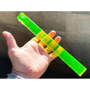 Op de afbeelding: Een neon groen en geel rechthoekig glazen object met een textuur. Het object heeft gele strepen en wordt in een hand gehouden.