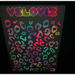 Può includere: Uno sfondo nero con un testo "VELOVIZ" arcobaleno in alto e un motivo di macchie di leopardo arcobaleno.