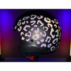 Könnte beinhalten: Ein schwarzer Motorradhelm mit einem weißen Leopardenmuster. Der Helm hat ein Visier und einen Kinnriemen.