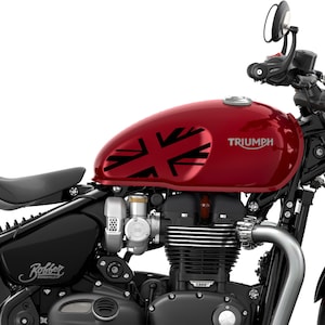 Puede incluir: Una motocicleta Triumph roja con un dise&ntilde;o de Union Jack negro en el tanque de gasolina. La motocicleta tiene un asiento negro y un manillar negro. La motocicleta es un modelo Bobber.