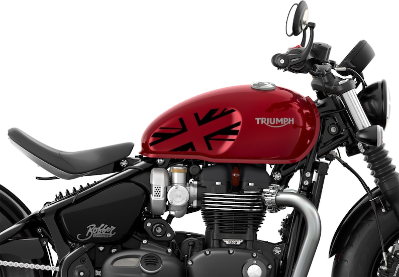 Puede incluir: Una motocicleta Triumph roja con un dise&ntilde;o de Union Jack negro en el tanque de gasolina. La motocicleta tiene un asiento negro y un manillar negro. La motocicleta es un modelo Bobber.