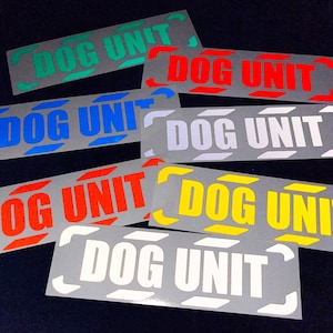May include: A collection of rectangular stickers with the text "DOG UNIT" in white, set against a gray background. The text is outlined with various colors, including red, green, blue, and yellow. The stickers have a reflective quality.
