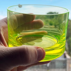 Peut inclure: Un verre gobelet en verre jaune néon translucide, de forme cylindrique avec une base plate. Le verre présente une surface lisse et polie ainsi qu'une teinte jaune citron vif et éclatante qui laisse passer la lumière, créant un effet lumineux.