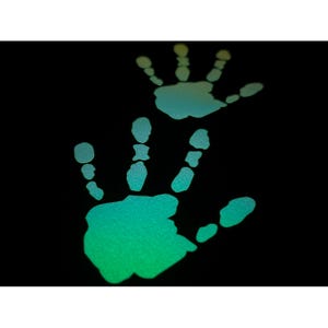 Pode incluir: Duas impressões de mãos luminosas, uma maior que a outra, num fundo preto. As impressões mudam de um verde vibrante para um azul suave, criando um efeito visual marcante. A imagem evoca temas de conexão e presença.