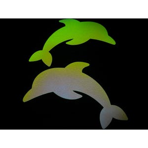 以下が含まれることがあります： 黒い背景に、鮮やかな緑と銀色のグラデーションのイルカのシルエットが2つ。イルカは、ひれと尾がはっきりと定義された、遊び心のある跳躍のポーズで描かれています。画像はキラキラした質感です。