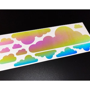 May include: A sheet of cloud-shaped stickers in various sizes. The stickers feature a gradient of colors, including yellow, pink, and blue. The stickers are on a white background.