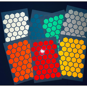 Può includere: Una collezione di adesivi colorati con motivo esagonale in vari colori, tra cui bianco, verde acqua, verde, argento, arancione, rosso e giallo. Gli adesivi sono disposti su uno sfondo blu scuro, mettendo in risalto le loro superfici riflettenti.