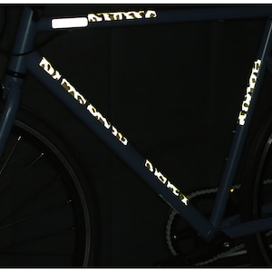 May include: A blue bicycle with reflective tape in a camouflage pattern on the frame. The tape is visible in the dark.