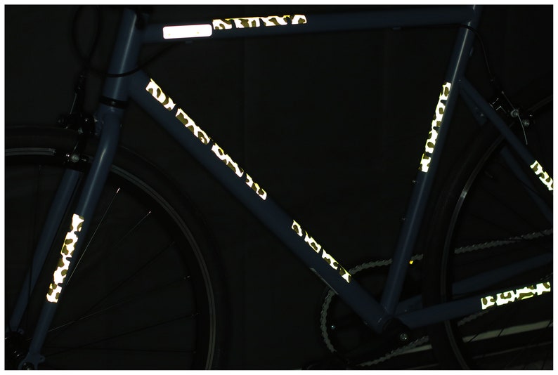 May include: A blue bicycle with reflective tape in a camouflage pattern on the frame. The tape is visible in the dark.