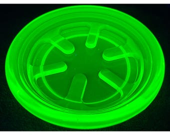 May include: A neon green, circular object with a series of curved cutouts. The object has a raised rim and a flat, textured interior. The bright green color gives it a glowing appearance against the dark background.