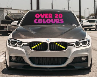 May include: A white BMW car with a black grille and yellow accents. The windshield has a sign that reads "OVER 20 COLOURS".