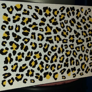 Puede incluir: Un fondo blanco con un estampado de leopardo negro y dorado.