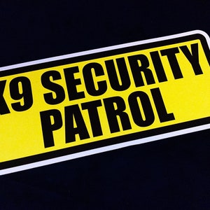 Peut inclure: Un panneau jaune et noir avec le texte "K9 SECURITY PATROL" dessus.
