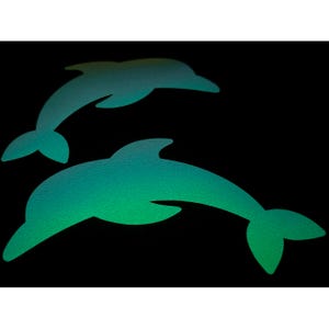 以下が含まれることがあります： 黒い背景に、2匹のティール色のイルカのシルエット。イルカはテクスチャ加工が施されており、ティールから緑への色のグラデーションがあります。イルカは反対方向に泳いでいます。