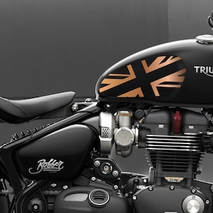 以下が含まれることがあります： ガソリンタンクに銅製のユニオンジャックのデザインが施された、黒いトライアンフ・ボンネビル・ボバーのオートバイ。オートバイは黒い革のシートとクロムメッキのエンジンを搭載しています。