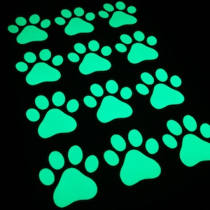 May include: A set of 12 glow-in-the-dark paw print stickers. The paw prints are a bright green colour and are arranged in a staggered pattern.