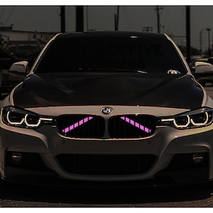 May include: A white BMW car with a black bonnet and pink LED lights in the front grille.