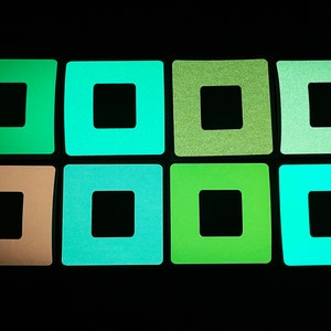 Könnte beinhalten: Acht quadratische, im Dunkeln leuchtende Aufkleber mit einem schwarzen Quadrat in der Mitte. Die Aufkleber sind in verschiedenen Grüntönen, Blau- und Brauntönen.