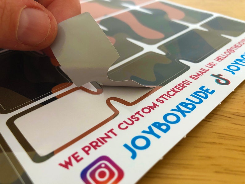 Puede incluir: Una hoja de pegatinas personalizadas con un patr&oacute;n de camuflaje. Las pegatinas tienen forma de bocadillos de di&aacute;logo. El texto en la hoja dice "WE PRINT CUSTOM STICKERS! EMAIL US: HELLO@THEJOYBOXBUDE.COM JOYBOXBUDE"