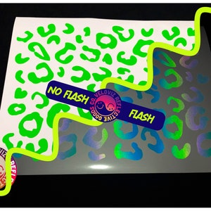 Puede incluir: Dos hojas de vinilo con un diseño de estampado de leopardo. Una hoja es verde y la otra es iridiscente. Las hojas están etiquetadas como "Sin flash" y "Flash" para mostrar cómo se ve el vinilo reflectante con y sin flash.