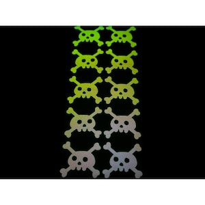 May include: A collection of skull and crossbones stickers in a variety of colors, including green, yellow, and silver. The stickers are arranged in vertical rows against a black background. The skull and crossbones design is a classic symbol.