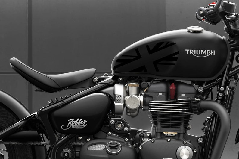 Puede incluir: Una motocicleta Triumph Bonneville Bobber negra con un dise&ntilde;o de Union Jack en el tanque de gasolina. La motocicleta tiene un asiento de cuero negro y un motor cromado.