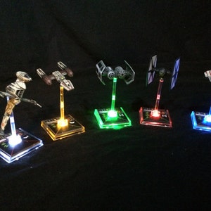 Puede incluir: Seis modelos de naves espaciales de Star Wars en soportes de exhibición iluminados. Los soportes son cuadrados y tienen una base de acrílico transparente con una luz que ilumina la base en diferentes colores. Los colores son blanco, amarillo, verde, rojo, azul y azul claro.