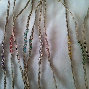 May include: Eight hemp bracelets with different colored beads. The bracelets are made of natural hemp cord and feature various colors of beads, including purple, red, black, turquoise, green, white, yellow, and black and green.