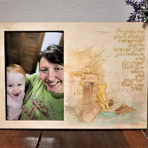 May include: A wooden picture frame featuring a photograph on the left and a Winnie the Pooh illustration with text on the right. The text reads "Promise me you'll always remember... braver than you believe, and stronger than you seem, and smarter than you think."