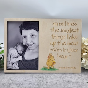 Op de afbeelding: Een houten fotolijst met een zwart-witfoto van een vrouw die een baby vasthoudt. De lijst heeft een Winnie de Poeh-citaat: "Soms nemen de kleinste dingen de meeste ruimte in je hart in."
