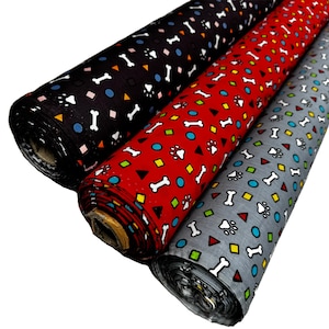 Op de afbeelding: Drie rollen stof met een herhalend patroon van witte botten, potafdrukken en kleurrijke geometrische vormen. De stof is zwart, rood en grijs.