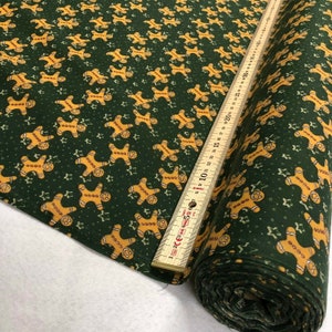 May include: A roll of green fabric with a repeating pattern of gingerbread men and stars. The fabric is measured with a ruler in centimetres.