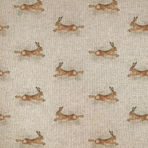 Può includere: Un motivo senza cuciture di lepri marroni che corrono su uno sfondo di lino beige.