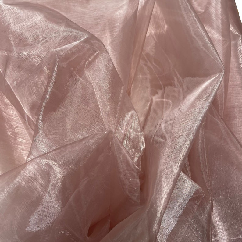May include: A sheer, pink fabric with a subtle shimmer. The fabric is draped and folded, creating a soft and delicate texture.