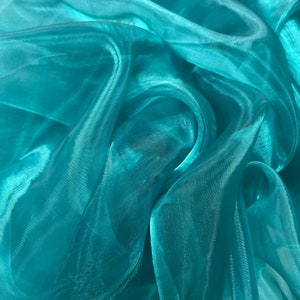 May include: Teal sheer fabric with a soft, flowing texture. The fabric is draped and folded, creating a sense of movement and depth.