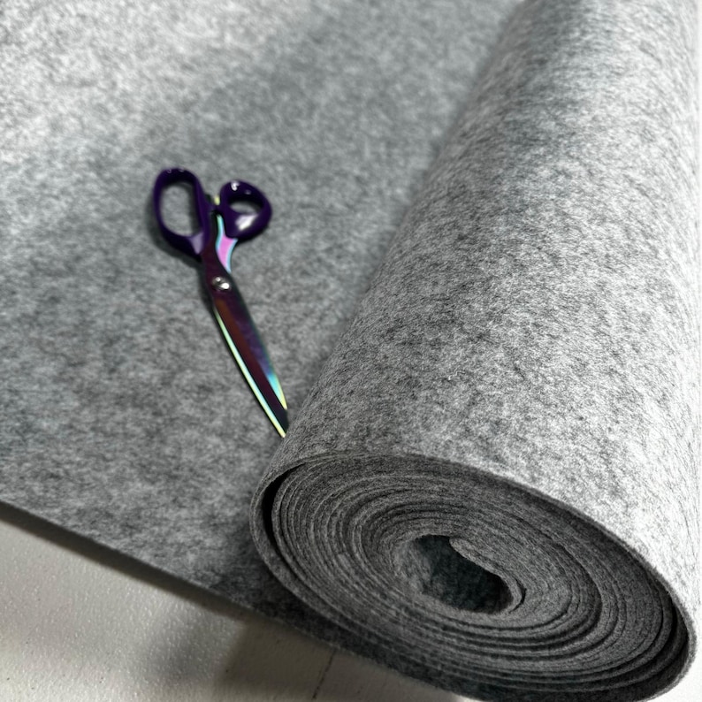 Puede incluir: Un rollo de tela de fieltro gris con un par de tijeras moradas en la parte superior.
