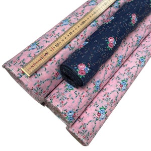 May include: Three rolls of fabric, one navy blue with white floral print and two pink with blue floral print. A wooden ruler is on top of the rolls.