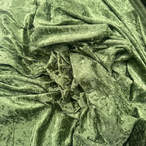 Puede incluir: Una pieza de tela de terciopelo arrugado en un color verde oliva intenso. El material presenta una textura irregular y distintiva con reflejos que captan la luz y sombras profundas creadas por los pliegues y drapeados sobre la superficie.